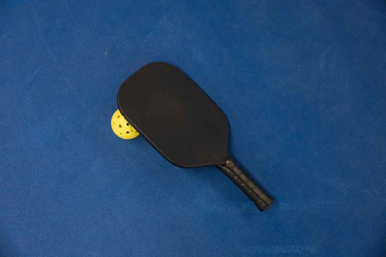 A pickleball paddle and ball on a textured blue surface, showcasing sports equipment.