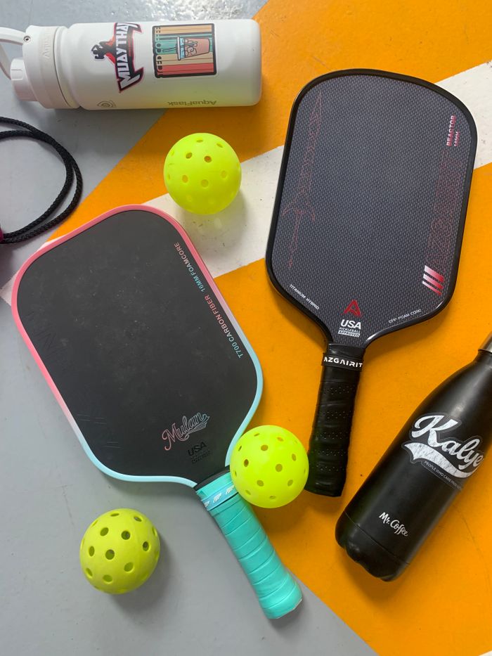Pickleball paddles and balls arranged with water bottles on a colorful floor.